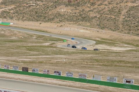 1995 Ford Taurus - Multiple vehicles navigate a turn on a race track surrounded by arid landscape.