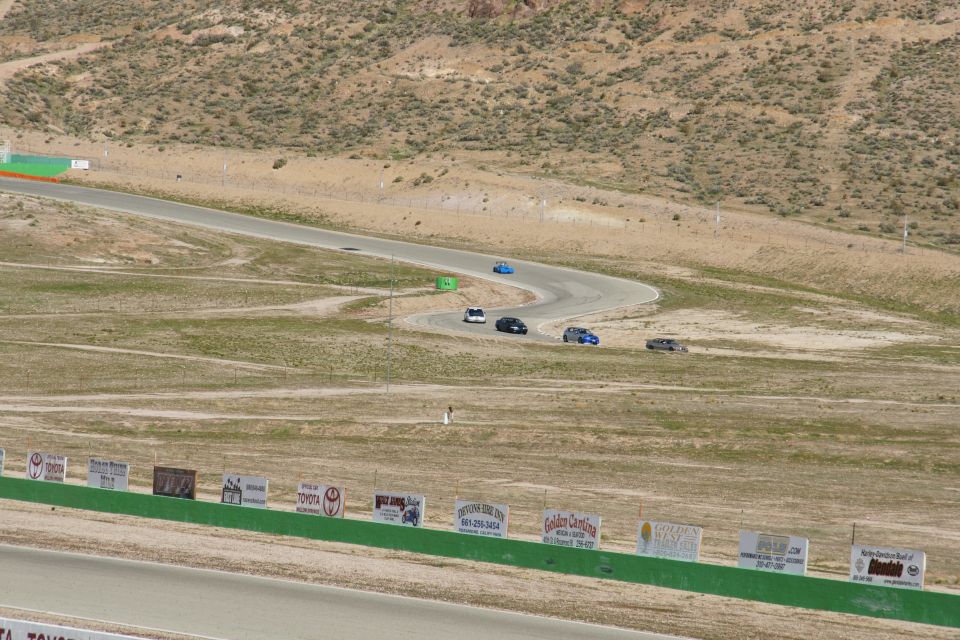Cars on a winding race track with dry, hilly terrain and advertising signs in the foreground