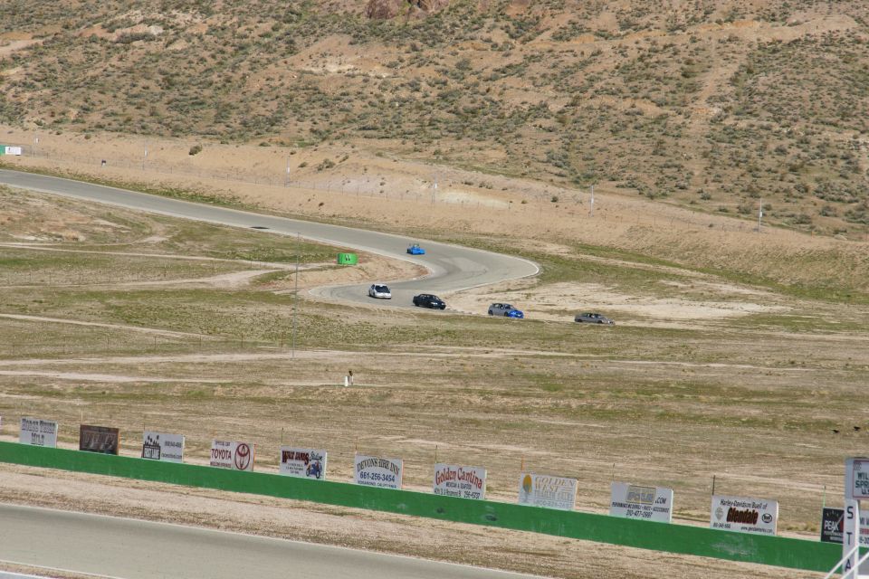 Several cars race on a winding track in a dry, hilly landscape