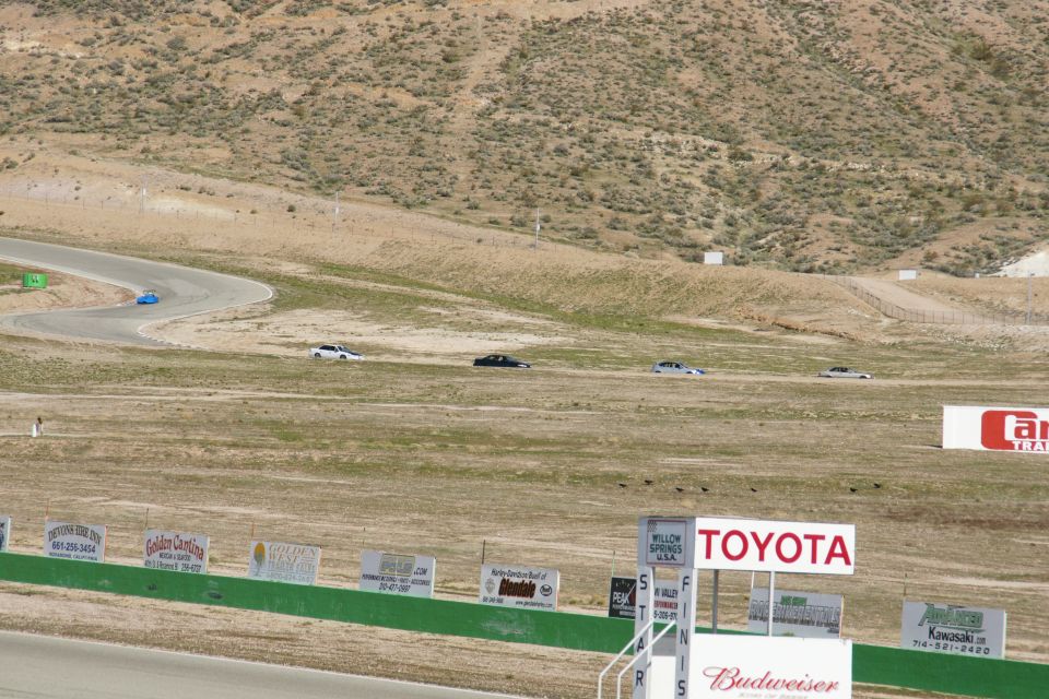 Cars on a winding race track with dry hills and advertising signs in the background