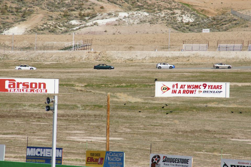 Four cars race on a track with hills in the background and advertisements