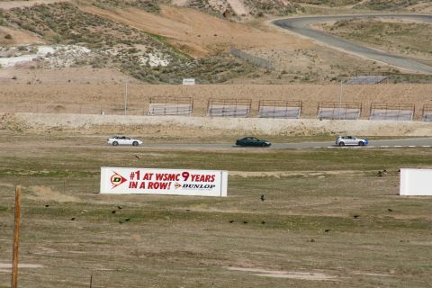 1995 Ford Taurus - A white sedan, a dark sedan, and a white hatchback are seen on a race track, with a large Dunlop advertisement in the foreground.