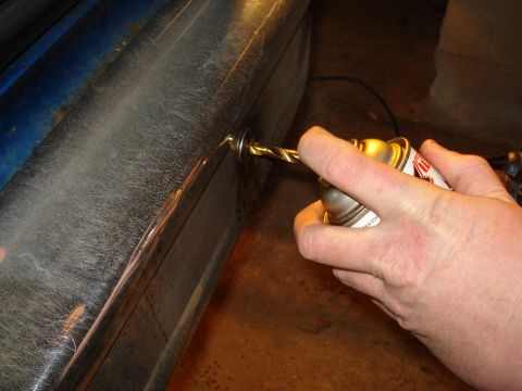 1985 Ford F-150 - A close-up shows a drill bit making a hole in a chrome bumper, with a spray can visible.