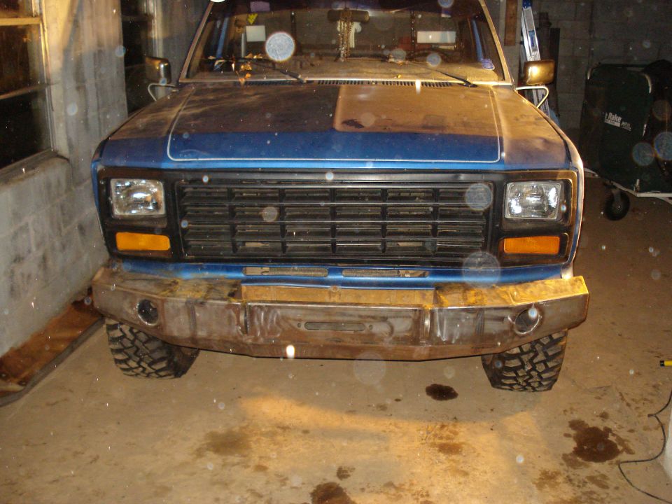 Front view of a blue pickup truck with a custom metal bumper and off-road tires, parked indoors