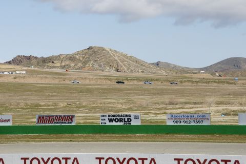 1995 Ford Taurus - A race track scene with several cars driving on it, set against a backdrop of hills and mountains.