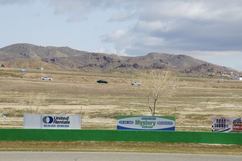 1995 Ford Taurus - A black car and a white car drive on a racetrack with a dry, hilly landscape and mountains behind them.