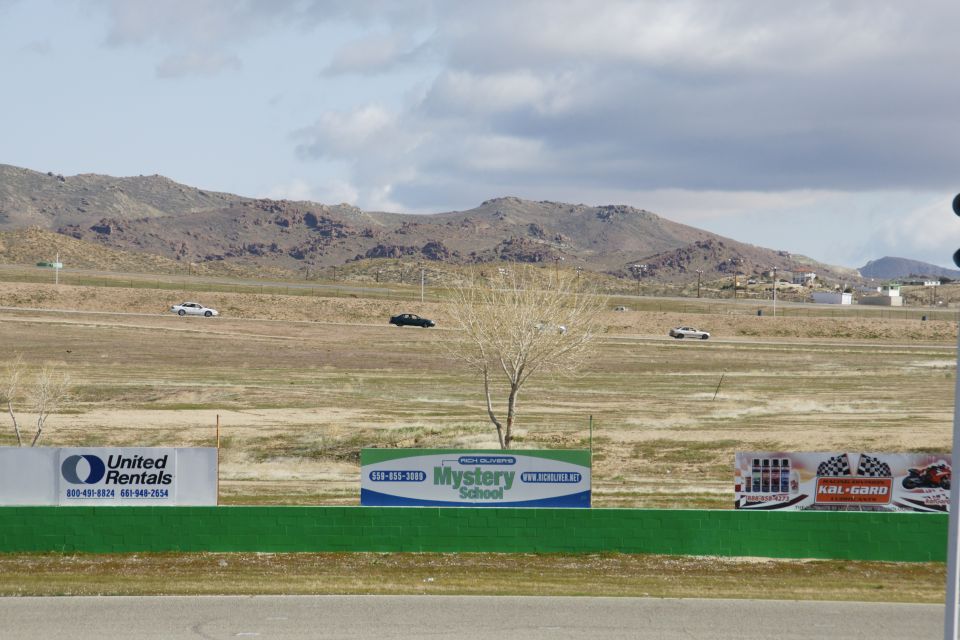 Race track with a few cars driving, mountains in the background, and advertising signs