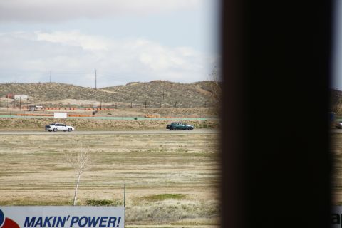 1995 Ford Taurus - Two cars on a racetrack under a cloudy sky. A sign in the foreground advertises 'MAKIN' POWER!'
