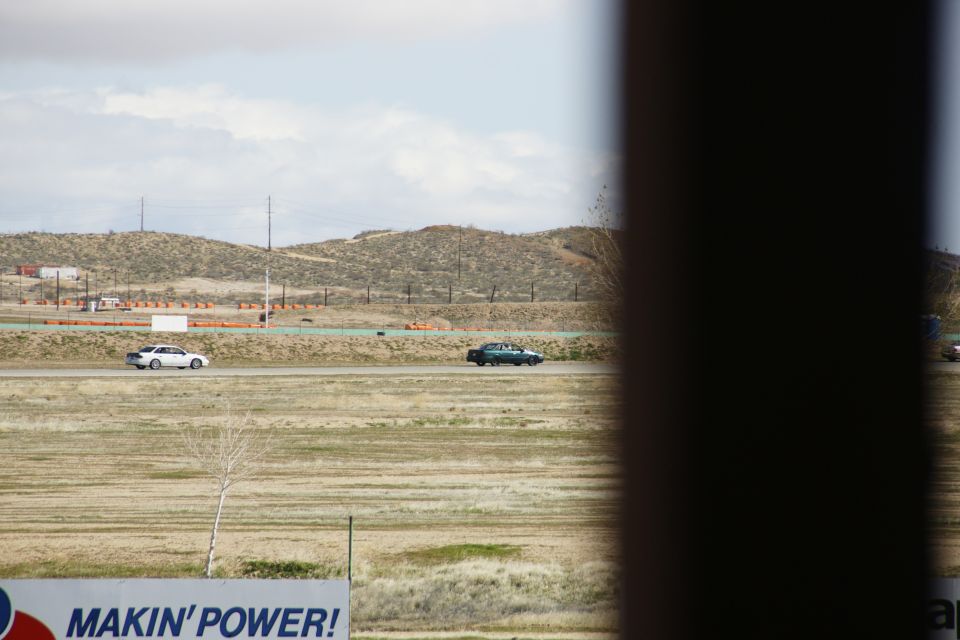 Two cars driving on a racetrack with hills in the background. A sign reads 'MAKIN' POWER!'