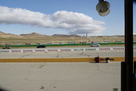 1995 Ford Taurus - Multiple vehicles race on a track under a cloudy sky, with banners and distant hills.