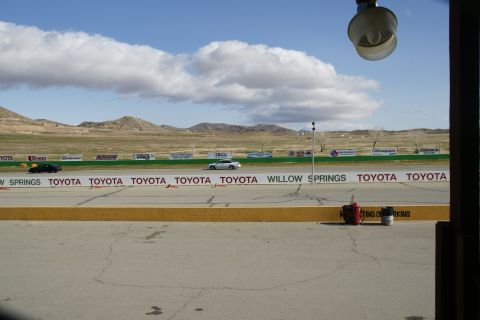 1995 Ford Taurus - A race track scene with two cars, Toyota sponsorship banners and distant hills under a cloudy sky.