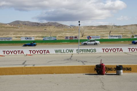 1995 Ford Taurus - A silver sedan drives on the Willow Springs race track, with a blue race car visible in the distance.