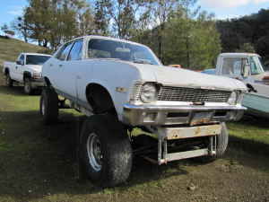 1991 Ford Bronco - A white sedan is heavily modified with a lift kit and oversized tires, with a truck and boat visible in the background.
