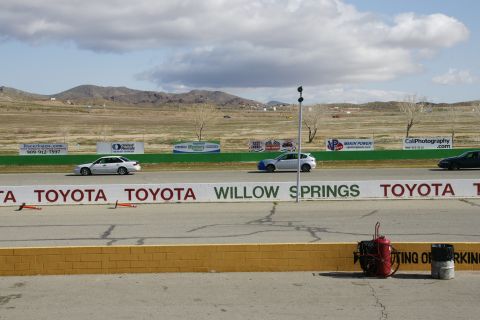 1995 Ford Taurus - Cars race on a track with sponsor banners and mountains in the background.