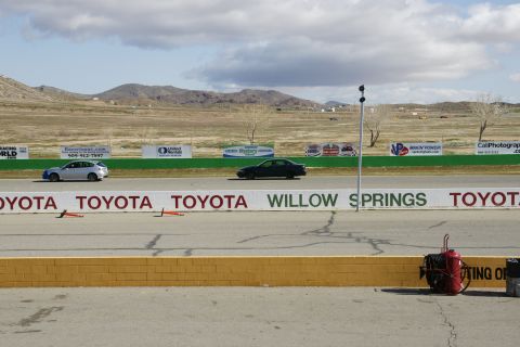 1995 Ford Taurus - A dark sedan is seen on the Willow Springs race track, with another vehicle visible further down the course.