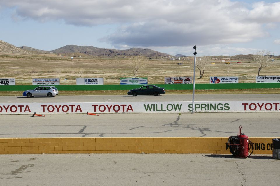 Dark sedan driving on a race track with a white car in the distance