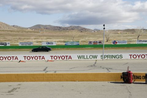 1995 Ford Taurus - A dark sedan drives on a racetrack, with various sponsor banners visible in the background.