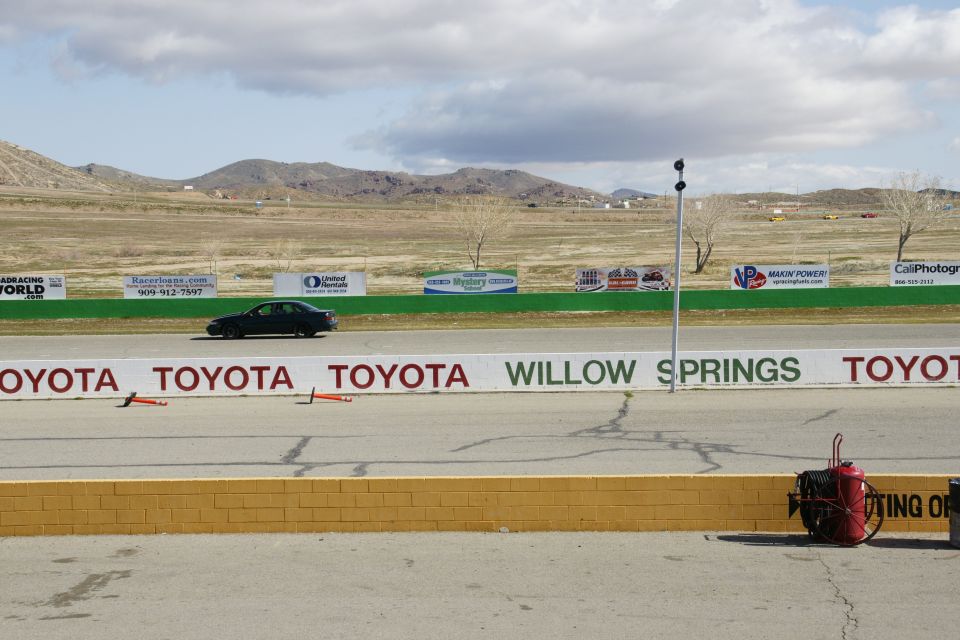 Dark sedan driving on a racetrack with Toyota and Willow Springs banners in the background