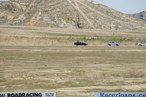 1995 Ford Taurus - Cars race on a track with a large mountain and dry grass surrounding it.