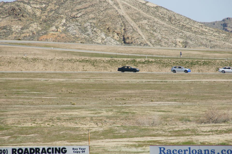 Three cars drive on a track with a mountain in the background