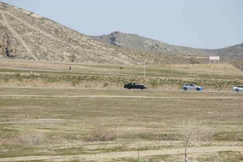 1995 Ford Taurus - Multiple vehicles travel along a road in a barren, mountainous region under a clear sky.