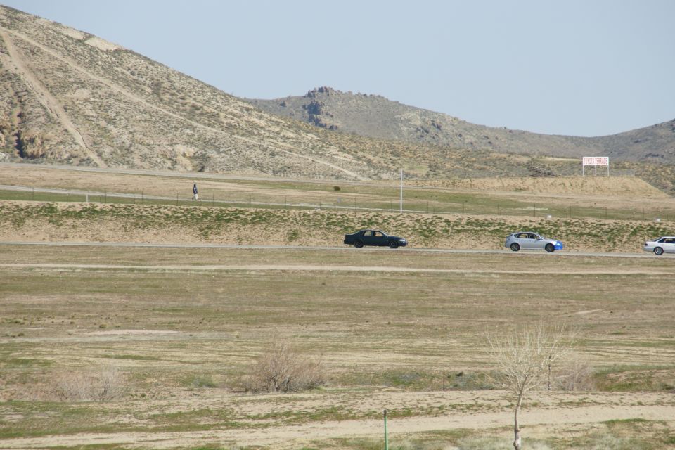 Three cars drive on a road in a dry, hilly landscape