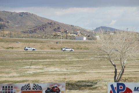 1995 Ford Taurus - Two white sedans are seen on a racetrack with a mountainous landscape under a cloudy sky.