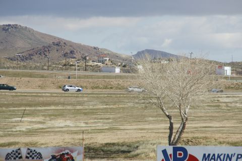 1995 Ford Taurus - Cars on a race track under a cloudy sky, with dry vegetation and distant buildings.