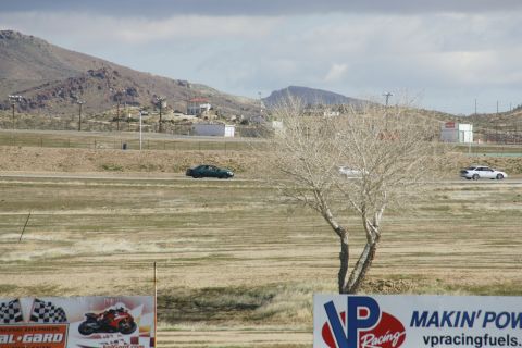 1995 Ford Taurus - A dark sedan and a white car are visible on a race track with mountains in the background.