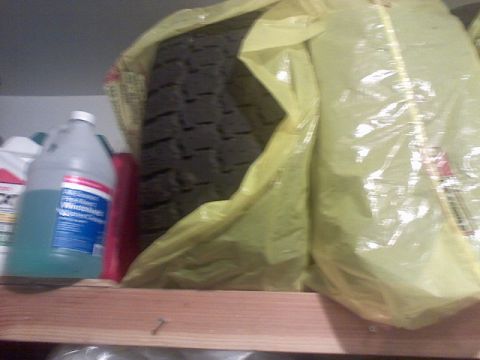 1996 Ford Bronco - A tire is stored in a yellow bag on a shelf with other automotive fluids.