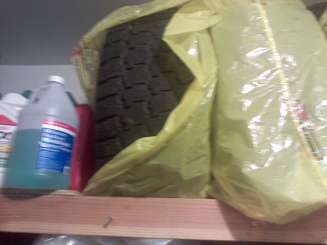 Tire stored in a yellow plastic bag on a shelf next to bottles of windshield washer fluid