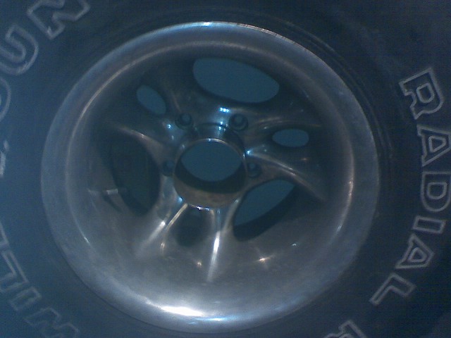 Close-up of a chrome alloy wheel with five spokes and a tire with raised lettering