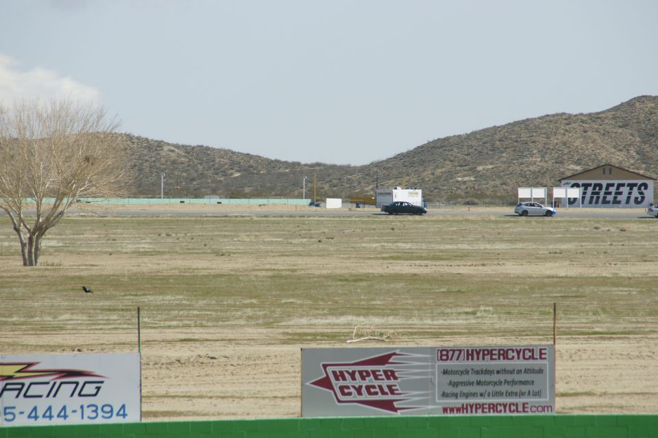Desert landscape with a race track, a few cars, a trailer, and buildings with 'STREETS' visible