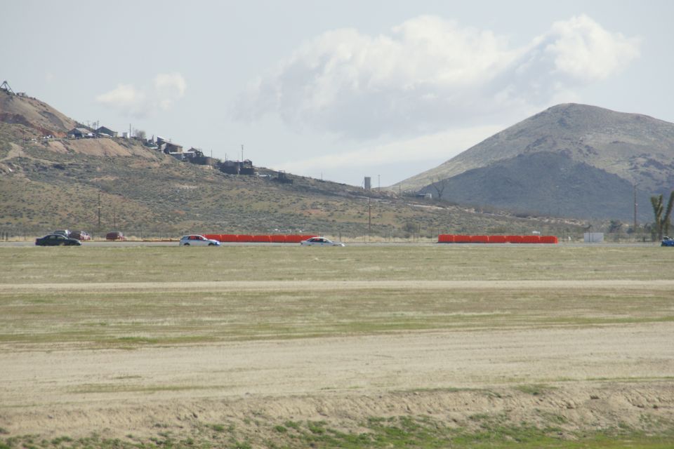 Several cars drive on a road with mountains and buildings in the background