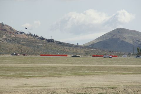 1995 Ford Taurus - Several cars are visible on a track with orange barriers, set against a backdrop of hills and a cloudy sky.
