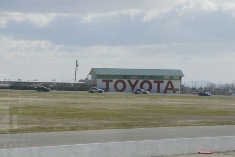 1995 Ford Taurus - Several vehicles are seen on a racetrack with a large TOYOTA sign visible on the building in the background.