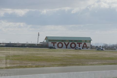 1995 Ford Taurus - Three cars drive past a large building with the TOYOTA logo on its side.