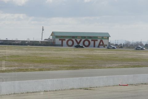1995 Ford Taurus - Cars drive on a track in front of a large building with "TOYOTA" painted on its side.
