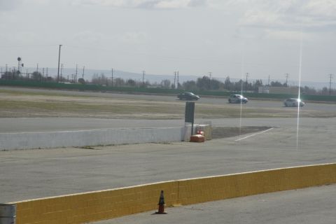 1995 Ford Taurus - Cars race on a track under a cloudy sky, with utility poles and distant trees visible.