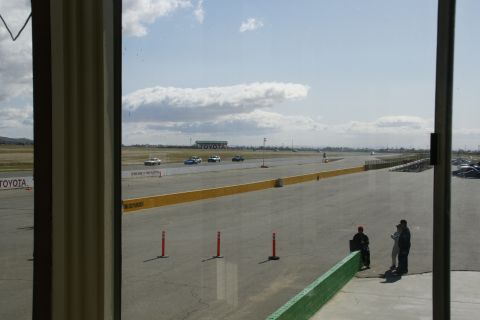 1995 Ford Taurus - A view of a race track with several cars in motion, under a partly cloudy sky. Toyota branding is visible in the background.
