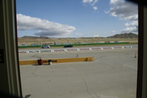 1995 Ford Taurus - Two cars drive on a track with a Toyota Willow Springs banner in the foreground.