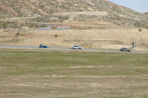 1995 Ford Taurus - Cars compete on a racetrack under a bright sky, with barren hills in the distance.