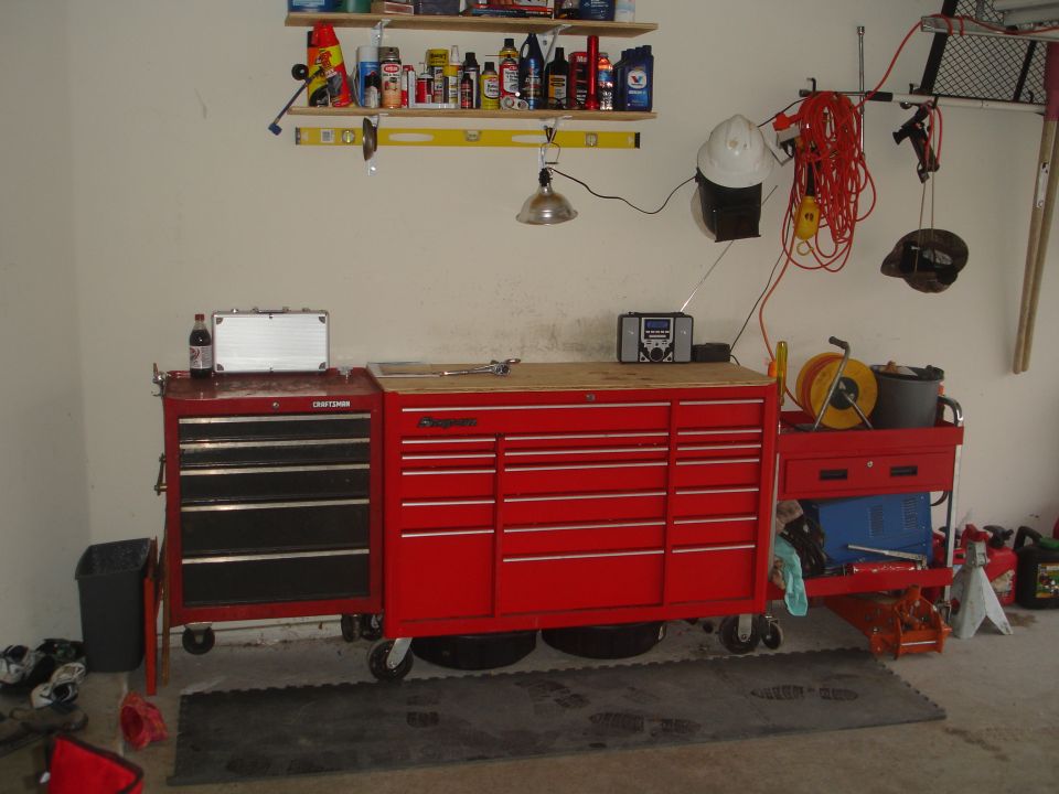 Red Craftsman and Snap-on tool chests with a workbench top, shelves with supplies above, and various garage items around