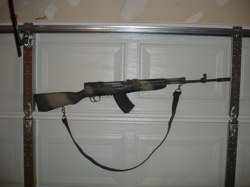 assault rifle with camouflage paint hanging on a garage door