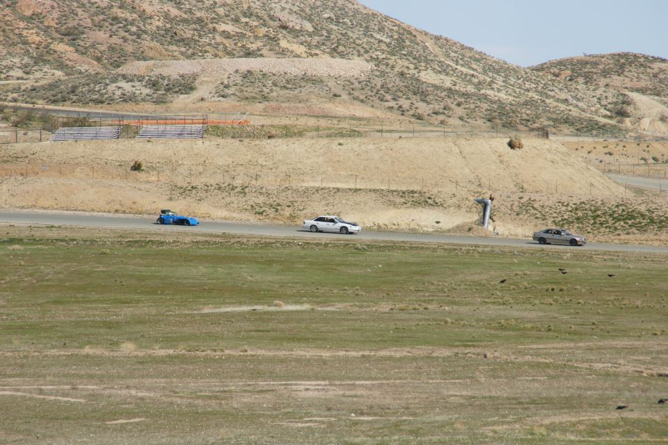 Silver sedan and blue race car on a paved track with dry hills in the background