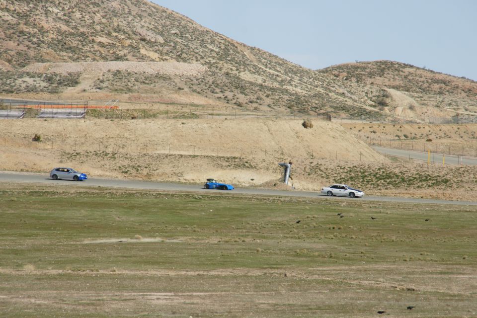 Three cars driving on a paved track with dry, hilly terrain in the background