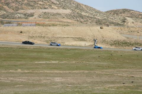 1995 Ford Taurus - Several cars are driving on a paved road in a dry, hilly landscape.