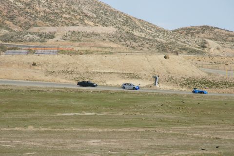 1995 Ford Taurus - A black car, a silver car, and a blue car race on a track surrounded by arid terrain.
