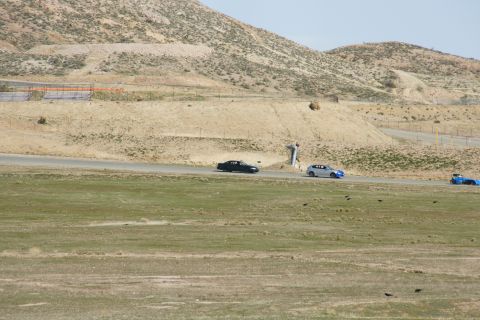 1995 Ford Taurus - A trio of cars navigate a turn on a desert racetrack under a clear sky.