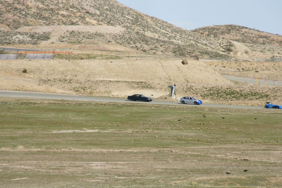 Three cars on a racetrack, one black, one white with blue accents, one blue
